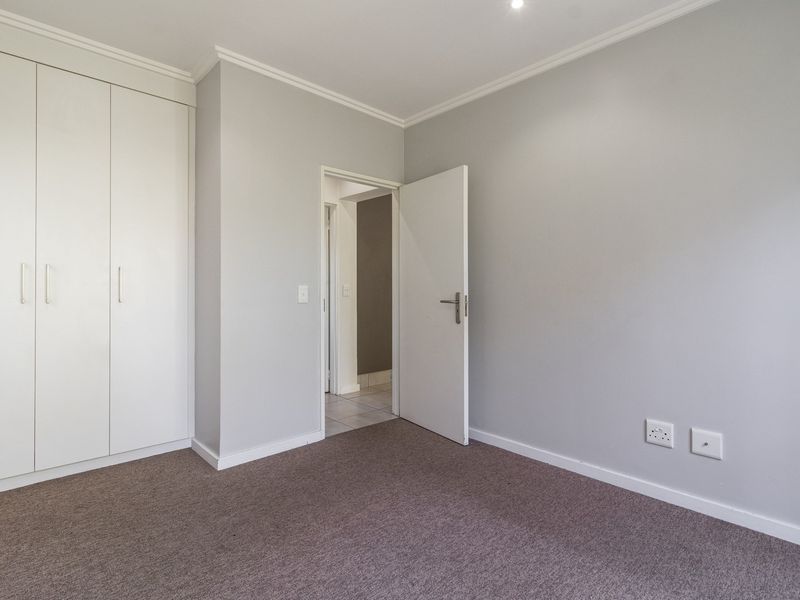 A clean, empty bedroom featuring neutral grey walls, carpeted flooring, and built-in white cupboards, offering a versatile space ready for personalization.