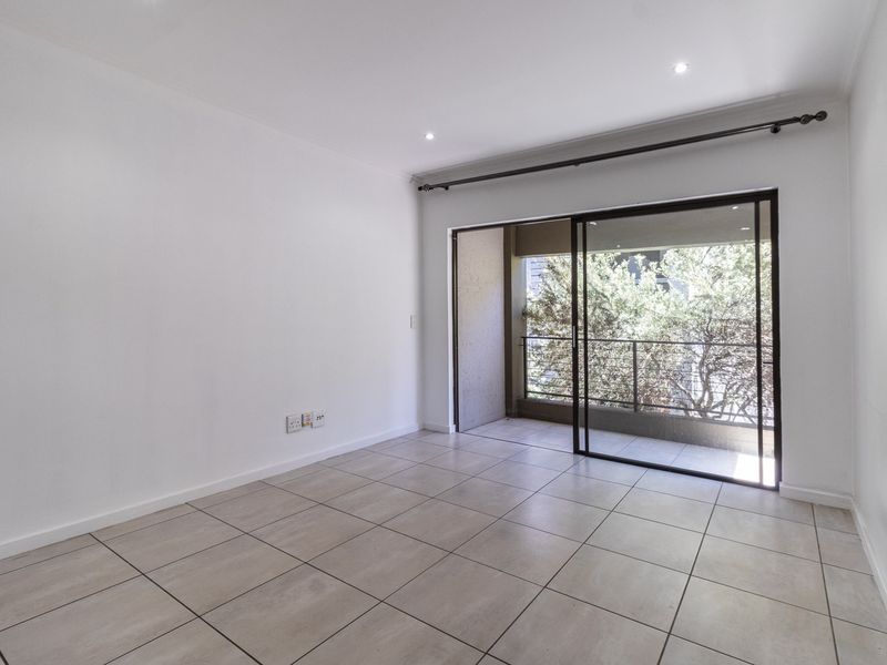 A bright, empty living room featuring neutral tiled flooring, recessed lighting, and a large sliding glass door providing access to a private balcony.