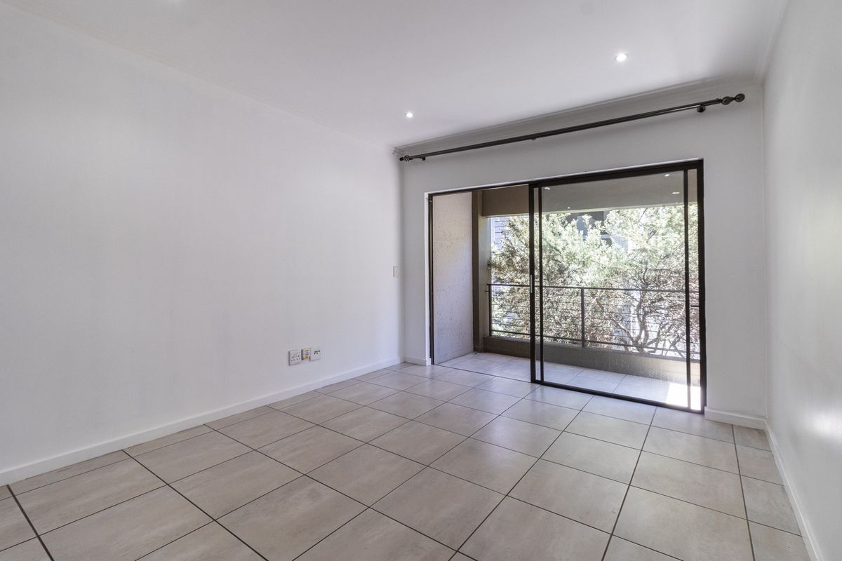 A bright, empty living room featuring neutral tiled flooring, recessed lighting, and a large sliding glass door providing access to a private balcony.