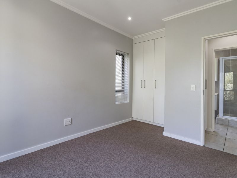 A clean, neutral bedroom featuring built-in cupboards, carpeted flooring, and direct access to an en-suite bathroom.