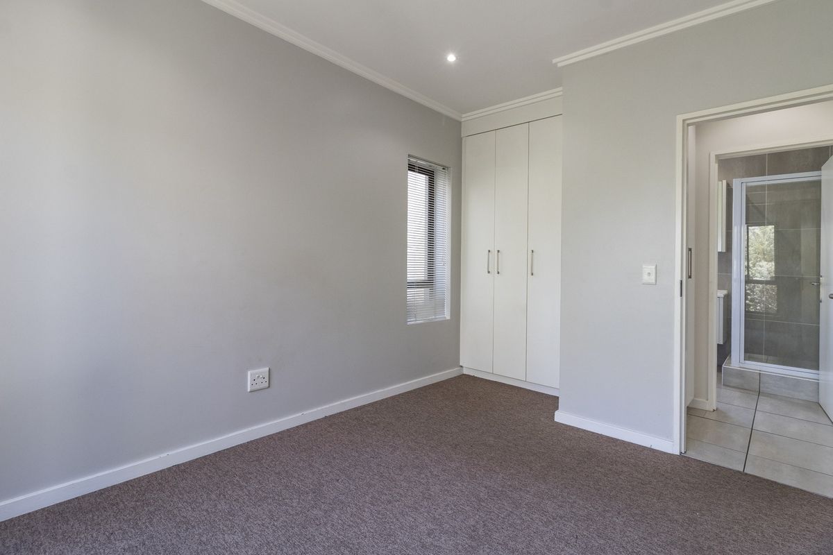 A clean, neutral bedroom featuring built-in cupboards, carpeted flooring, and direct access to an en-suite bathroom.