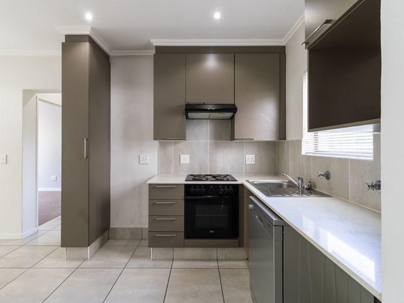 Modern kitchen featuring sleek cabinetry, built-in electric oven and hob, stainless steel sink, and neutral tiled finishes.