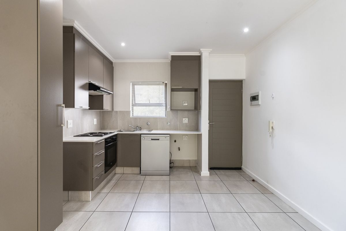 Modern kitchen featuring sleek grey cabinetry, built-in oven and hob, tiled flooring, and a neutral tiled backsplash in a clean, open-plan layout.