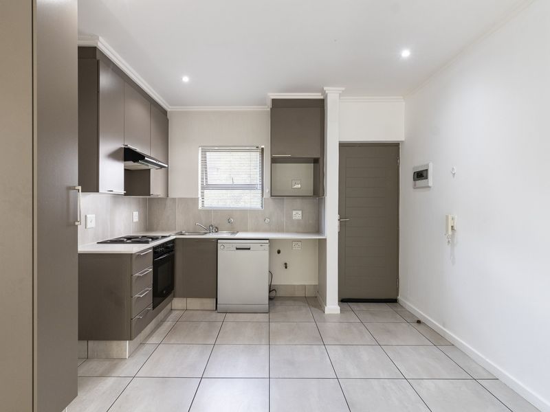 Modern kitchen featuring sleek grey cabinetry, built-in oven and hob, tiled flooring, and a neutral tiled backsplash in a clean, open-plan layout.