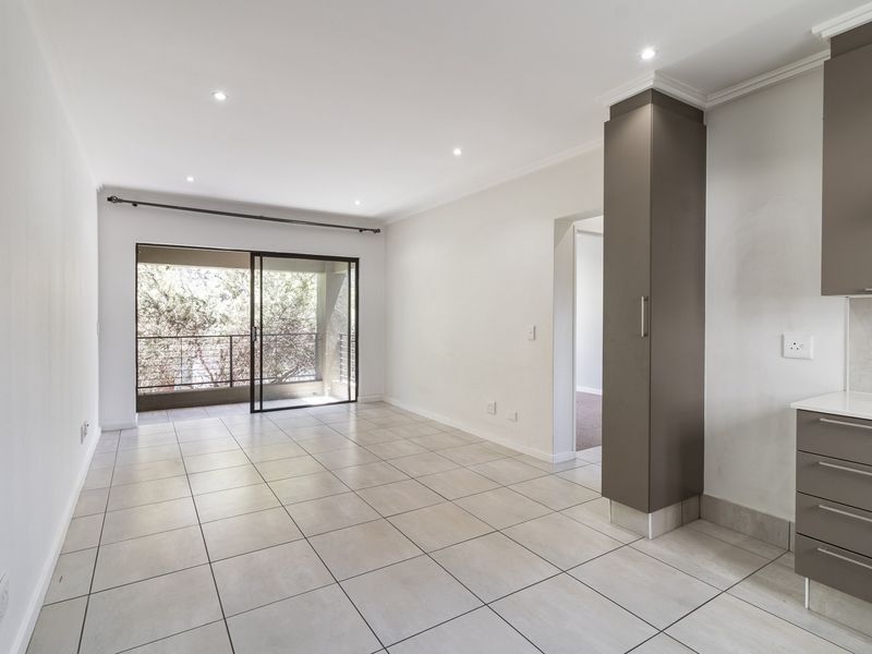 Bright open-plan living area featuring neutral tiled flooring, modern cabinetry, and direct access to a private balcony through sliding glass doors.