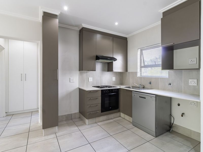 A clean, modern kitchen featuring neutral-toned cabinetry, built-in oven and hob, tiled backsplash, and ample storage space, presented in a bright, well-maintained condition.