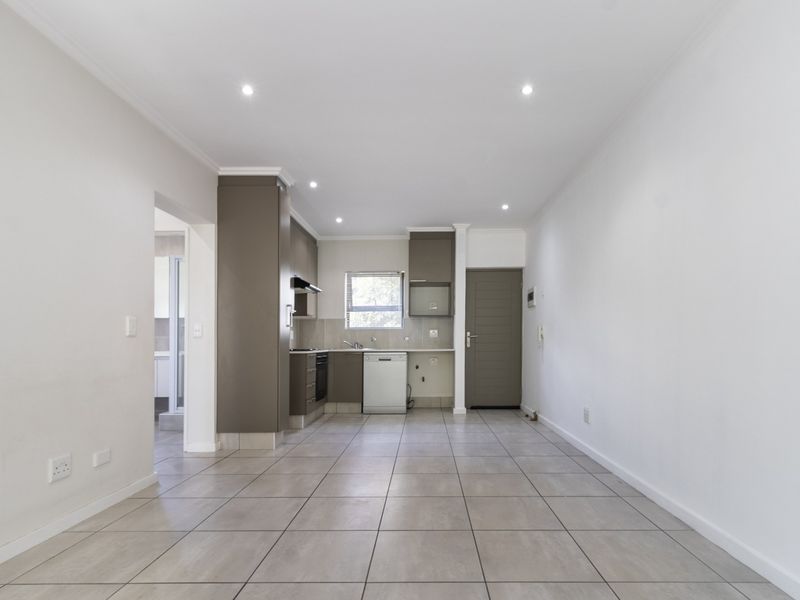 An open-plan living and kitchen area featuring neutral tiled flooring, recessed lighting, and modern built-in cabinetry with integrated kitchen appliances.