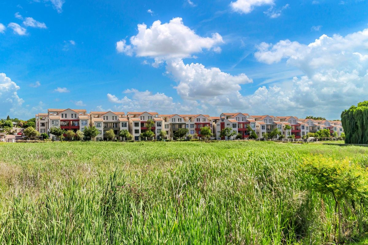 A wide-angle view of a multi-story apartment complex featuring terracotta roof tiles and balconies, set against a natural grassy landscape.