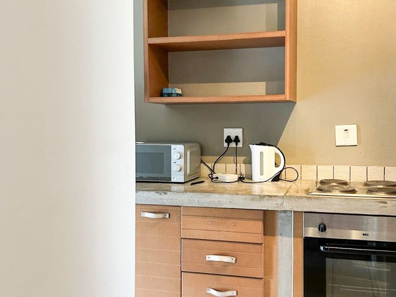 A compact kitchen featuring built-in oven, electric hob, concrete countertops, and laminate cabinetry with open shelving.
