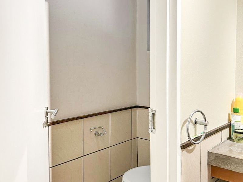 A compact bathroom featuring tiled walls and flooring, a standard toilet, and a vanity countertop with integrated towel ring.