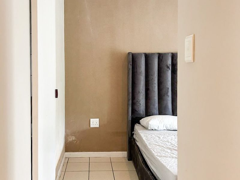 A bedroom featuring tiled flooring and a built-in cupboard, showing signs of wear on the wall finish.