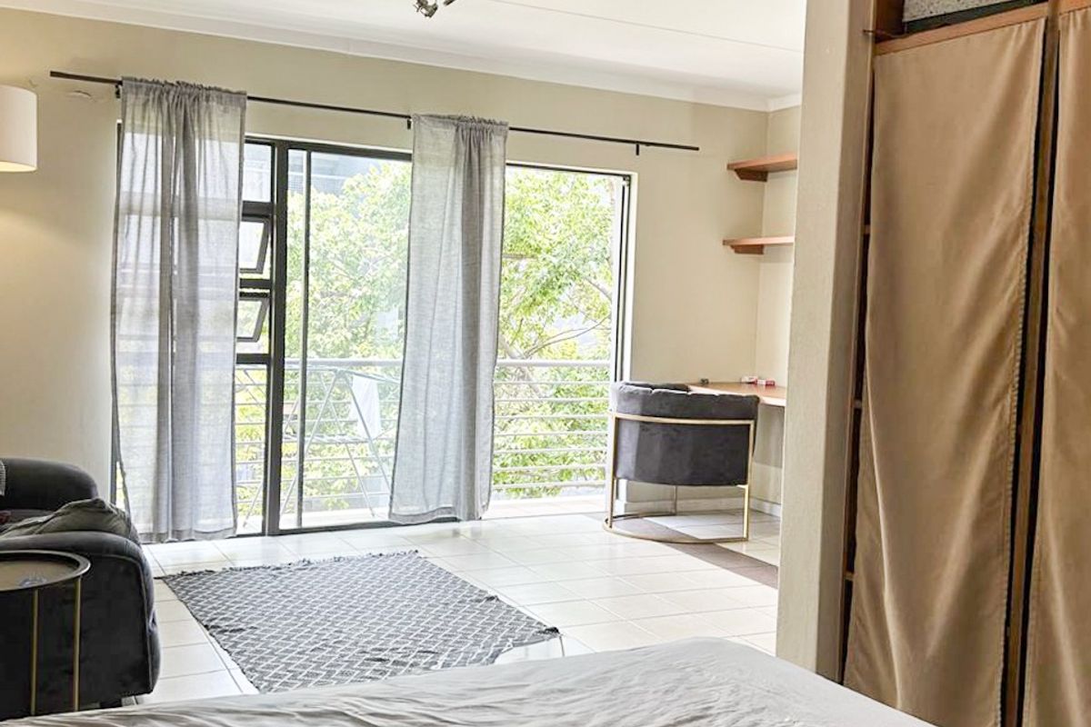 Spacious bedroom featuring built-in wardrobes, tiled flooring, and a sliding glass door leading to a private balcony with natural light.