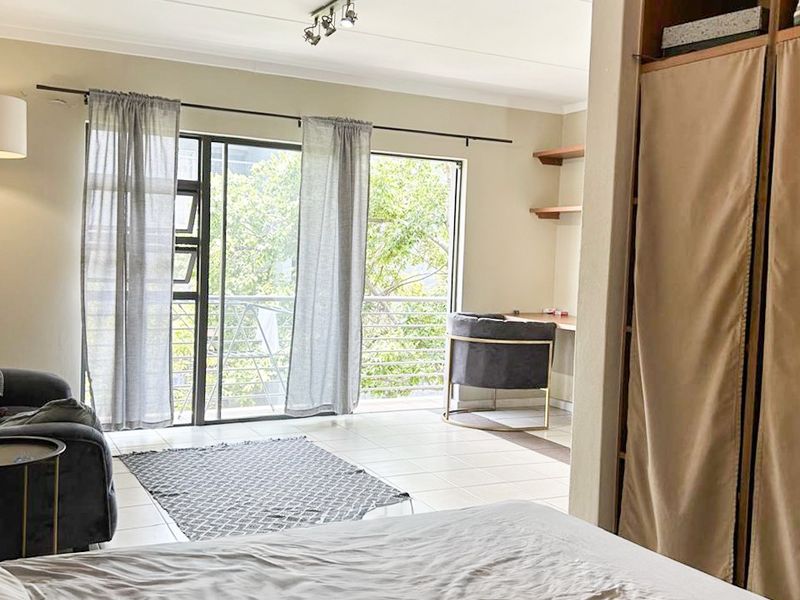 Spacious bedroom featuring built-in wardrobes, tiled flooring, and a sliding glass door leading to a private balcony with natural light.
