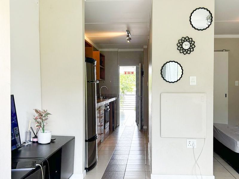 Open plan living area featuring tiled floors and a galley-style kitchen with built-in cabinetry and appliances, leading to an exterior doorway.