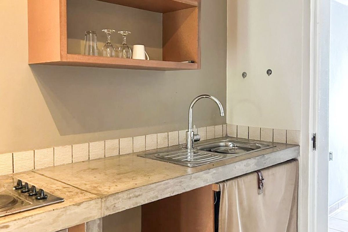 A compact kitchen area featuring a concrete countertop, built-in oven, hob, and open shelving, currently requiring finishing touches to the cabinetry.
