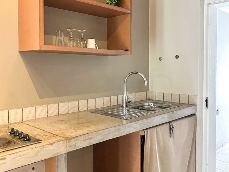 A compact kitchen area featuring a concrete countertop, built-in oven, hob, and open shelving, currently requiring finishing touches to the cabinetry.