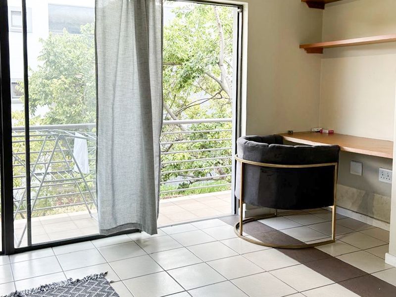 A functional home office space featuring a built-in desk, floating shelving, tiled flooring, and direct access to a private balcony through sliding glass doors.