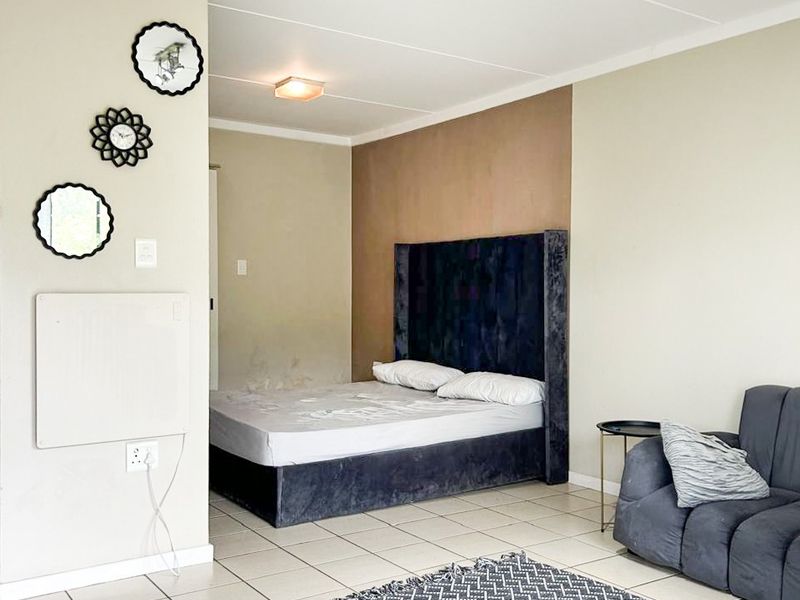 A bedroom featuring tiled flooring, wall-mounted heating, and ceiling track lighting, with visible wall imperfections requiring maintenance.