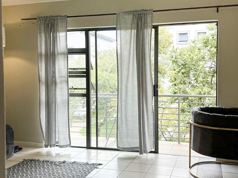Bright living area featuring tiled floors, track lighting, and large sliding glass doors opening onto a balcony with outdoor views.