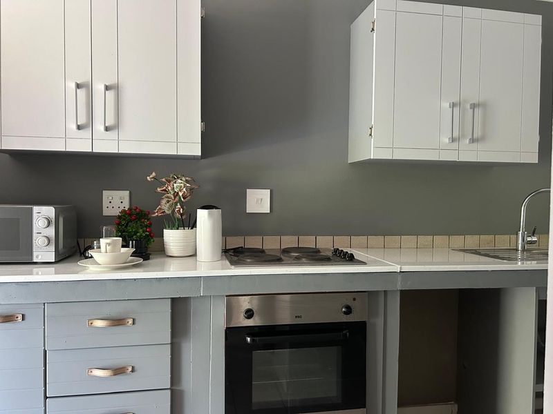 A functional kitchen area featuring built-in cabinetry, an electric hob, an integrated oven, and a stainless steel sink with a tiled backsplash.