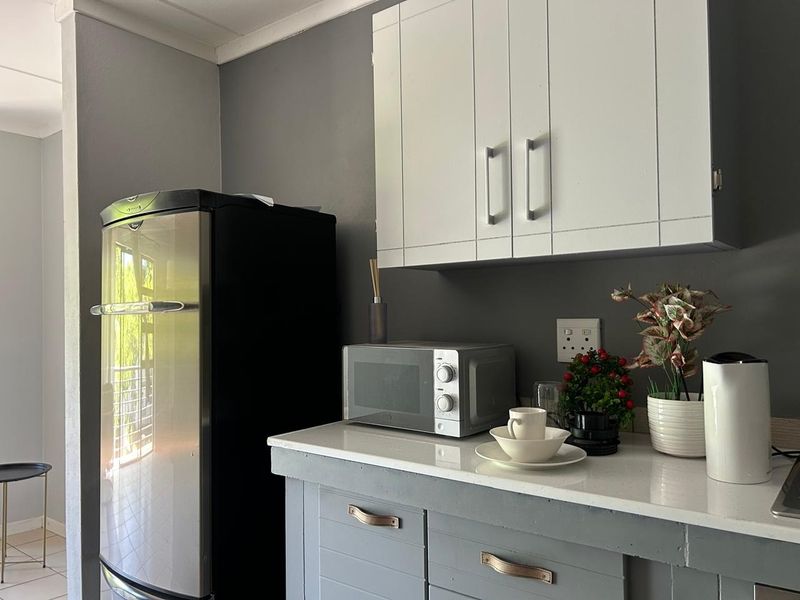 A compact kitchen area featuring grey cabinetry, white stone countertops, and modern wall-mounted storage units.