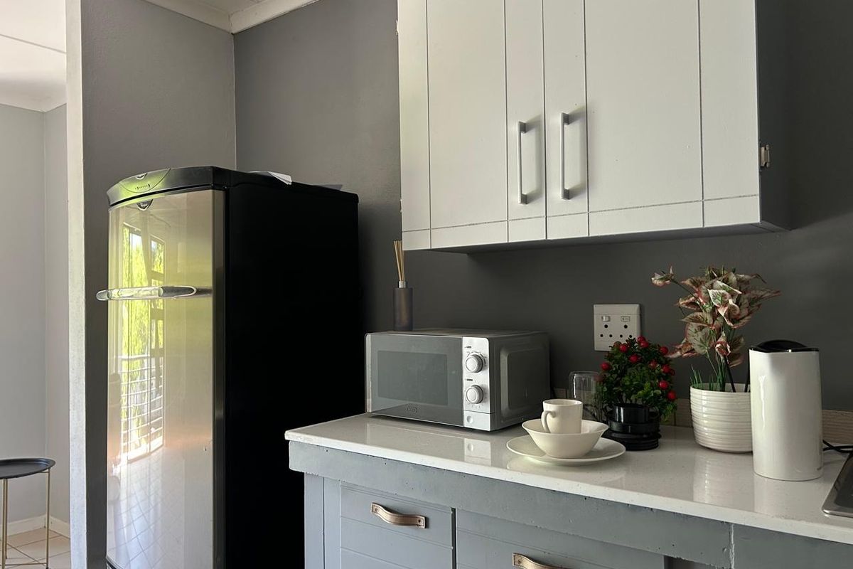 A compact kitchen area featuring grey cabinetry, white stone countertops, and modern wall-mounted storage units.