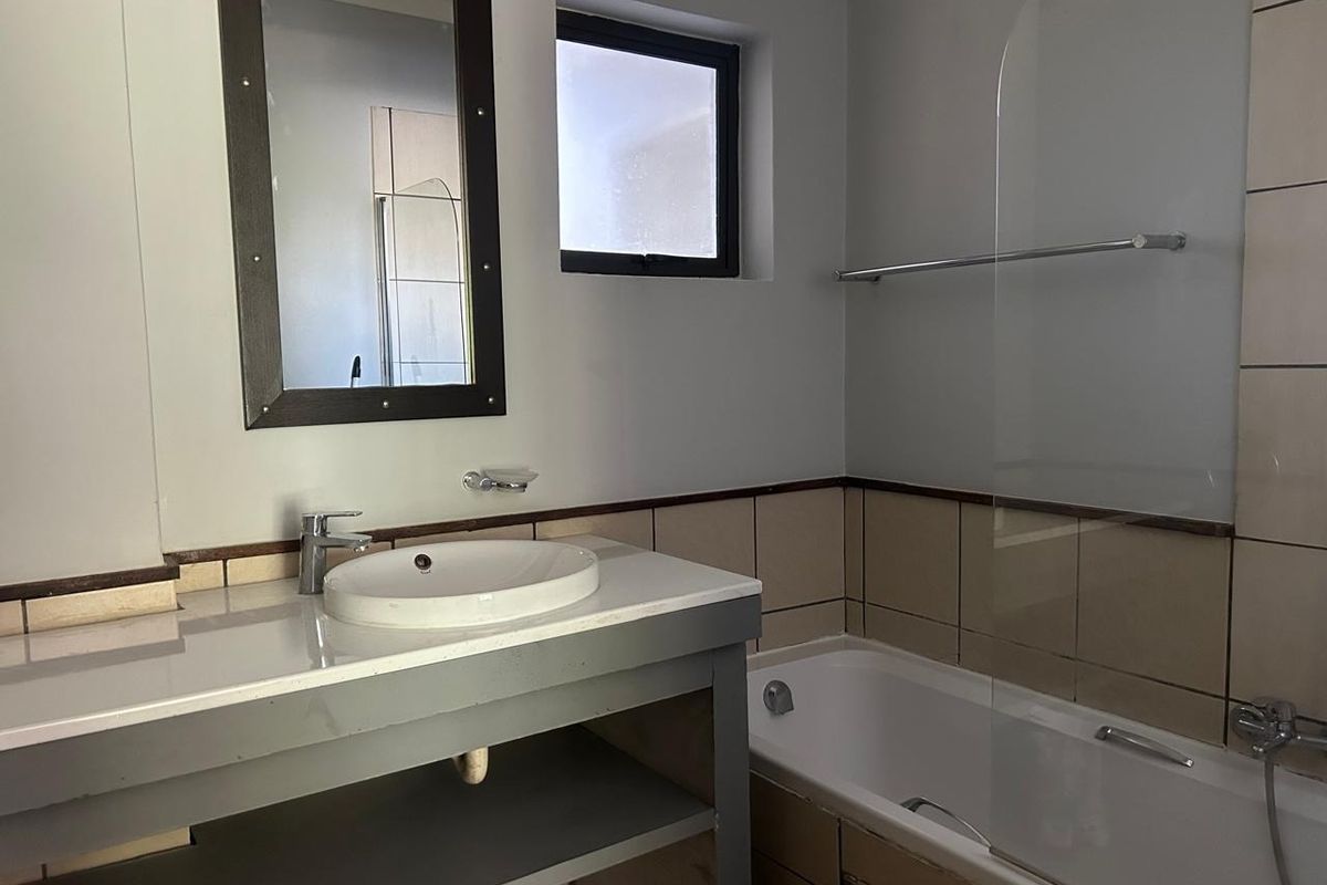 A functional bathroom featuring a vanity basin, bathtub with a glass shower screen, and tiled splashbacks, offering a clean and practical layout.