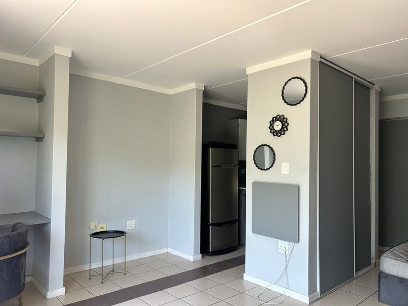 Open plan living area featuring tiled flooring, built-in shelving, and a modern sliding door wardrobe, providing a functional and versatile space.