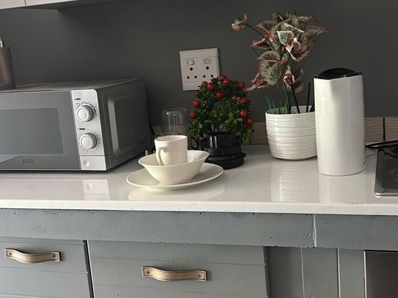 A compact kitchen area featuring grey painted cabinetry, a white stone countertop, and integrated oven, showing signs of wear on the drawer finishes.