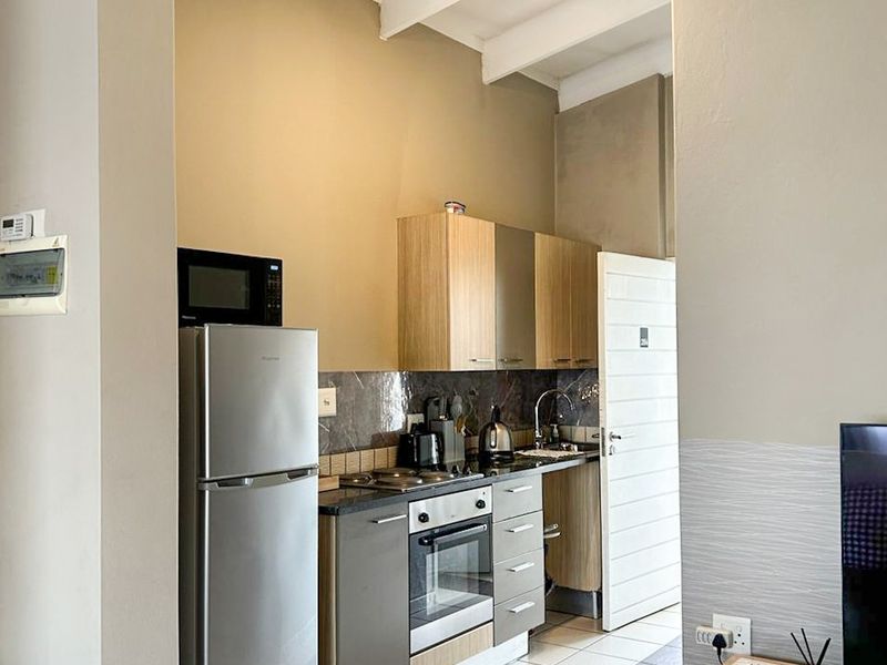 Compact kitchen featuring built-in cabinetry, an electric hob, oven, and tiled flooring, set within an open-plan living area with exposed ceiling beams.
