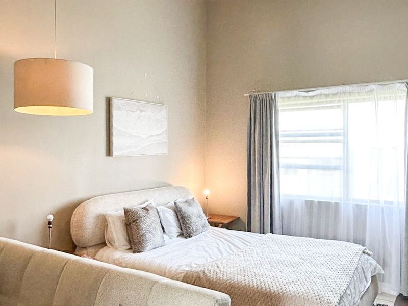 A well-lit bedroom featuring high ceilings with exposed beams, neutral wall tones, and large windows allowing for natural light.