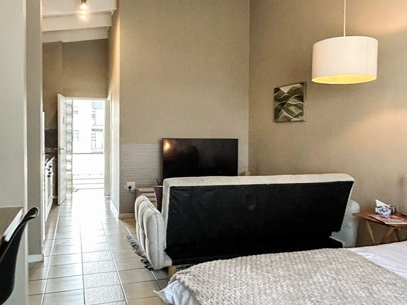 Open-plan living area featuring high ceilings with exposed beams, tiled flooring, and direct access to an outdoor balcony space.