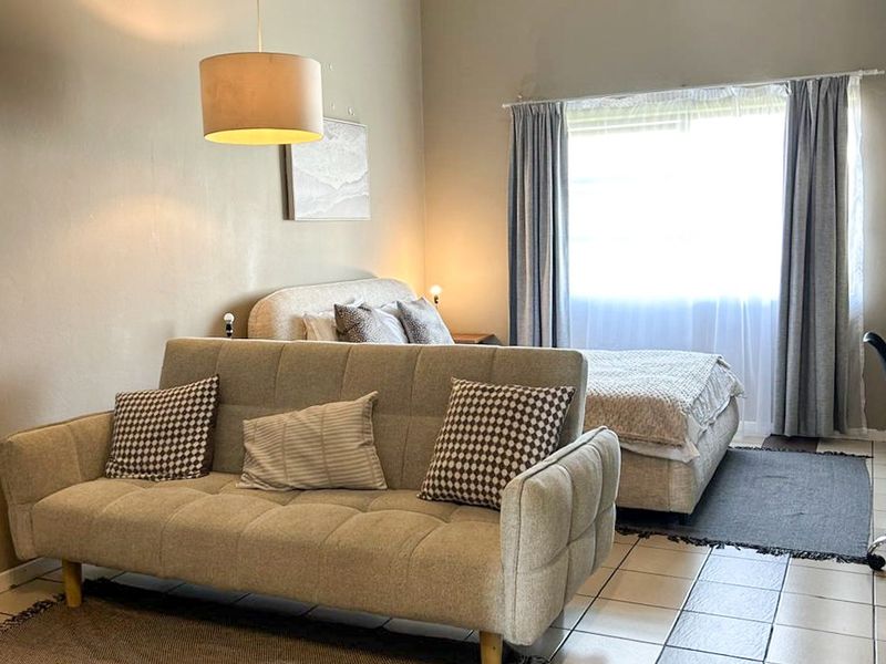 An open-plan living and bedroom area featuring high ceilings with exposed beams, tiled flooring, and neutral wall finishes.