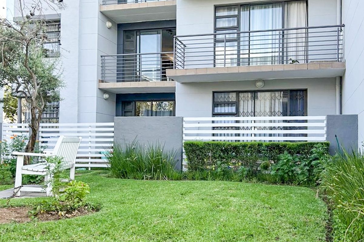 A view of the rear apartment facade featuring multiple balconies with metal railings, sliding glass doors, and a well-maintained private garden area.