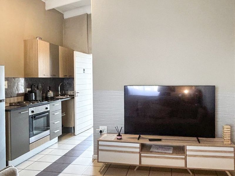 Open-plan living area featuring a compact kitchen with built-in cabinetry, oven, and hob, complemented by tiled flooring and exposed ceiling beams.