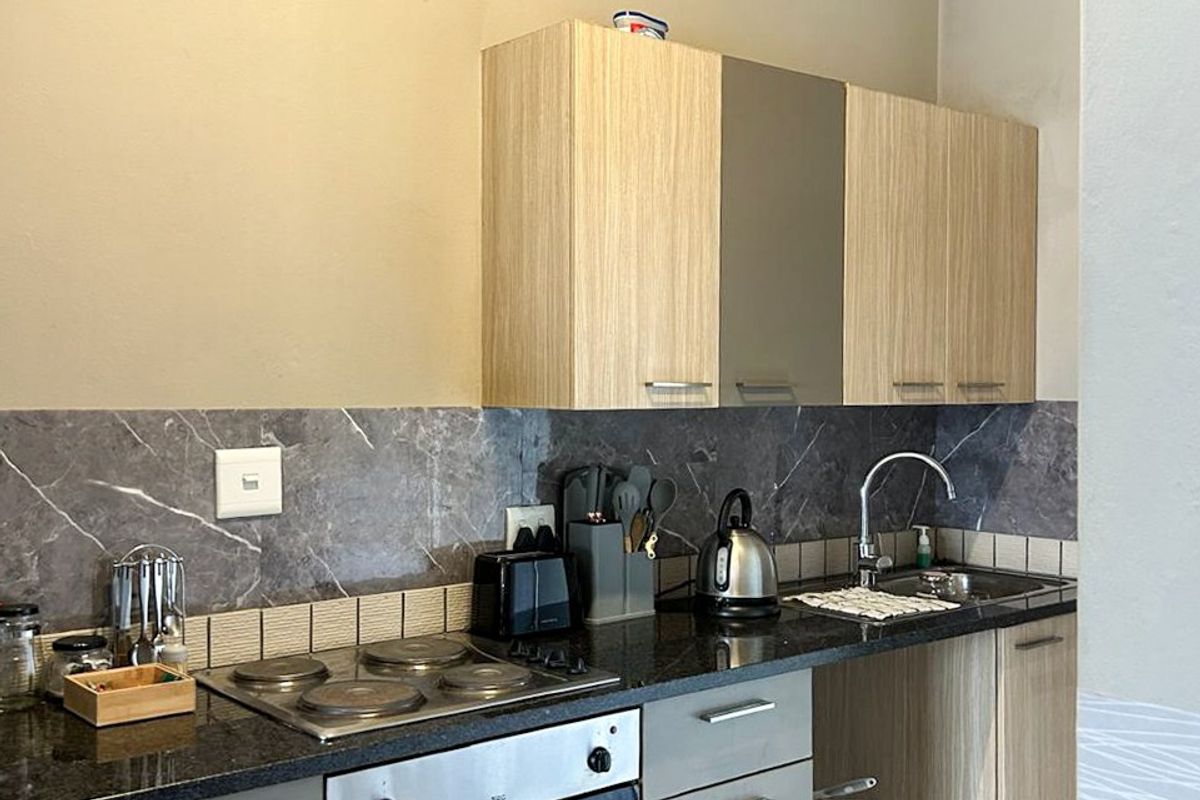 Compact kitchen featuring light wood-tone cabinetry, dark stone countertops, a built-in electric oven and hob, and a modern tiled backsplash.