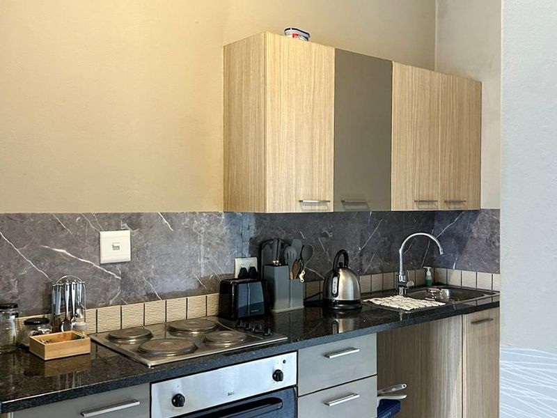 Compact kitchen featuring light wood-tone cabinetry, dark stone countertops, a built-in electric oven and hob, and a modern tiled backsplash.