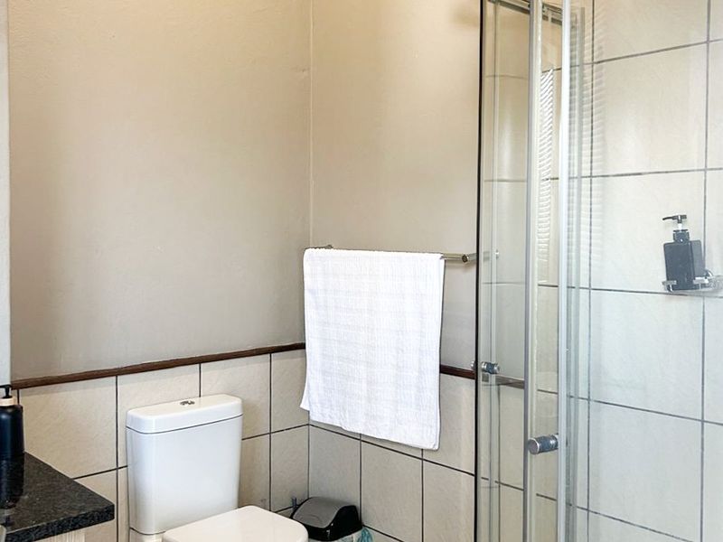 A functional bathroom featuring a corner shower enclosure, toilet, and vanity cabinet with a granite countertop.