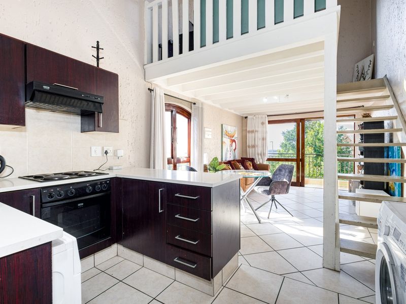 Open-plan kitchen and living area featuring dark wood cabinetry, tiled floors, and a staircase leading to a mezzanine level with balcony access.