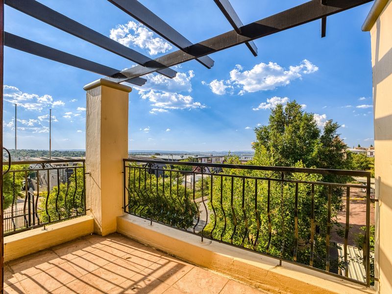 A spacious balcony featuring a pergola, wrought iron railings, and tiled flooring, offering expansive views of the surrounding area.