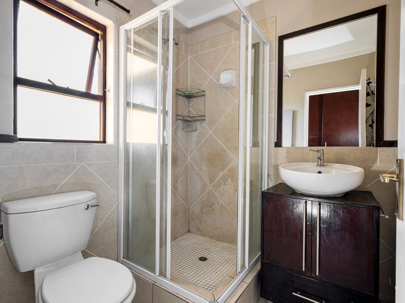 A functional bathroom featuring a shower enclosure, vessel sink with vanity cabinet, and tiled finishes, offering potential for cosmetic updates.