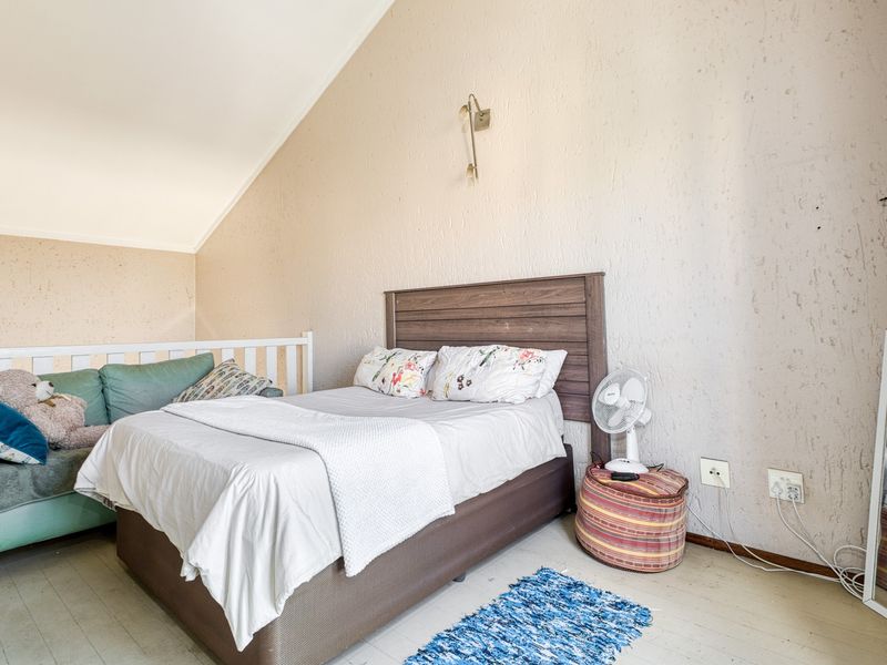 A bedroom featuring a vaulted ceiling and textured walls, providing a cozy atmosphere with functional wall-mounted lighting and accessible electrical outlets.