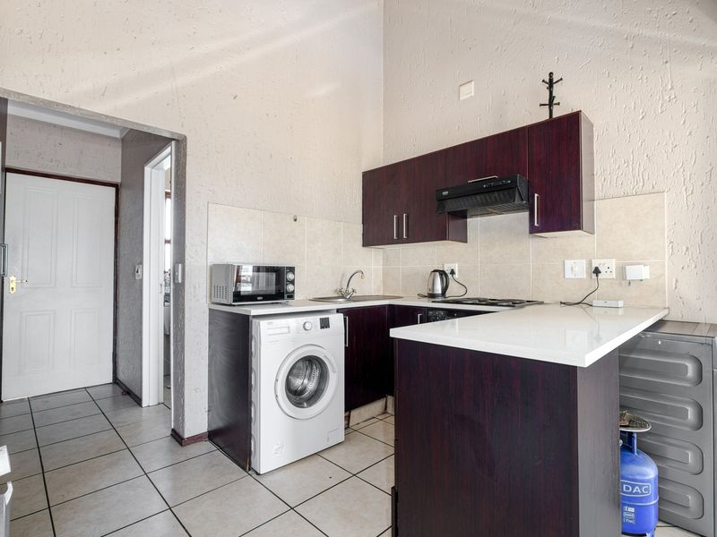 Compact kitchen featuring dark wood cabinetry, white stone countertops, tiled flooring, and integrated laundry plumbing, offering a functional layout for apartment living.