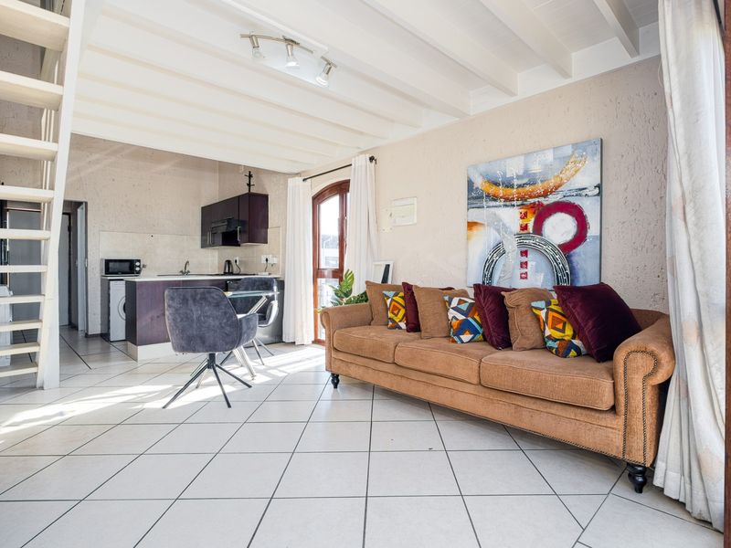 Open-plan living area featuring tiled floors, exposed beam ceilings, and an integrated kitchen space with a staircase leading to the upper level.