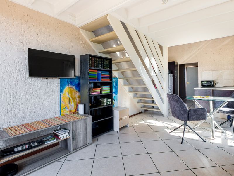 Open plan living and kitchen area featuring tiled flooring, a central staircase, and textured wall finishes in a functional apartment layout.