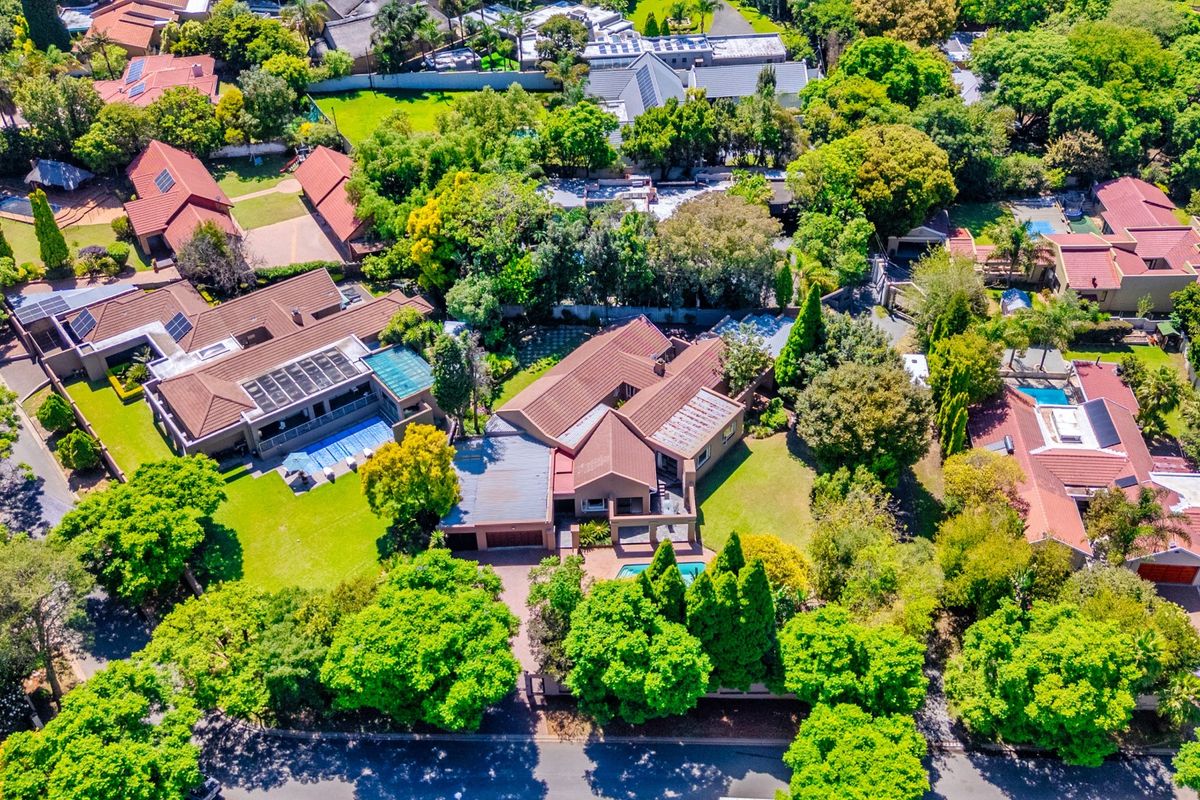 Aerial view of a residential property featuring a tiled roof, swimming pool, and established garden within a leafy suburban neighborhood.
