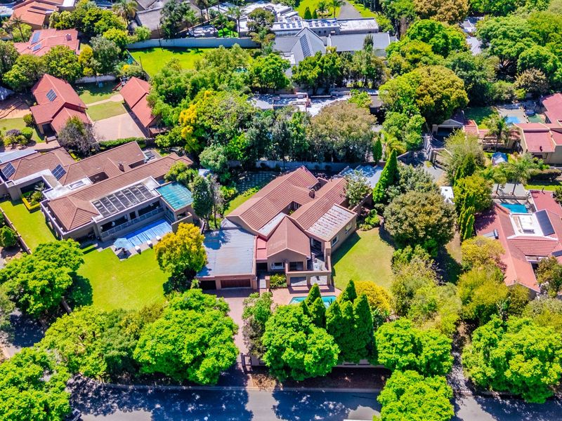 Aerial view of a residential property featuring a tiled roof, swimming pool, and established garden within a leafy suburban neighborhood.