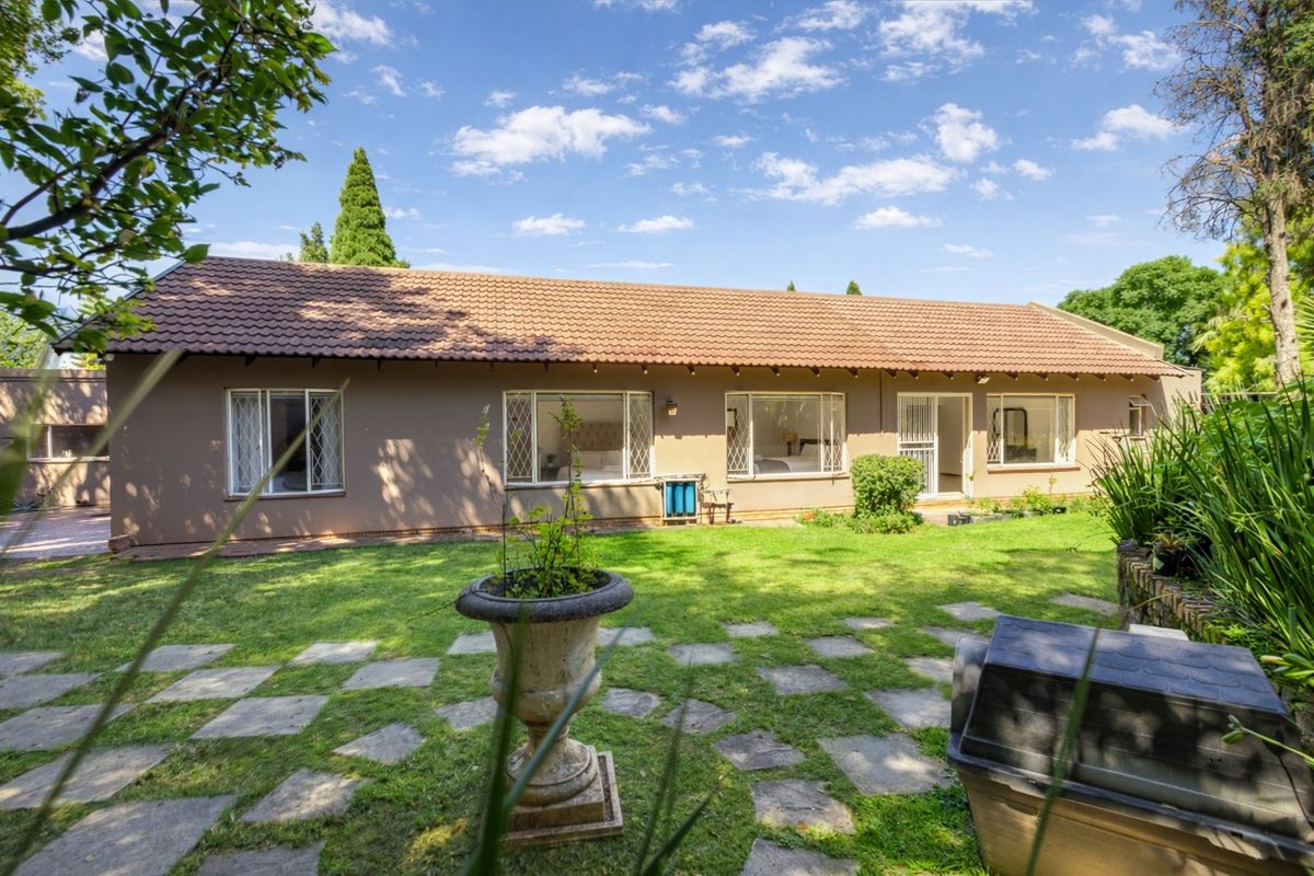 Rear view of the house featuring a tiled roof, metal window frames, and a garden with a paved walkway.