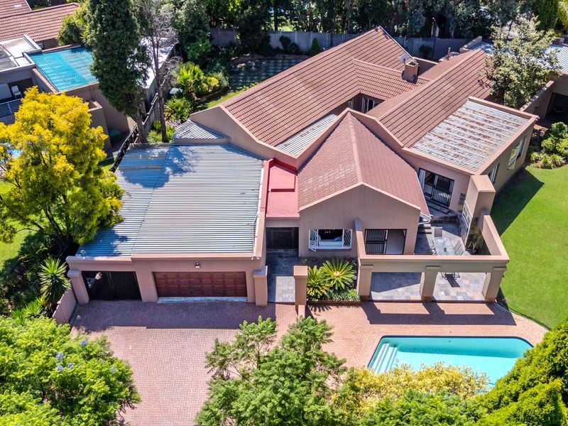 Aerial view of a residential property featuring a tiled roof, swimming pool, paved driveway, garage, and a spacious garden with a covered patio area.