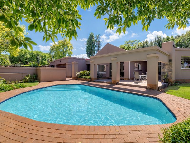 A well-maintained outdoor area featuring a swimming pool with brick paving and a covered patio with a built-in fireplace.